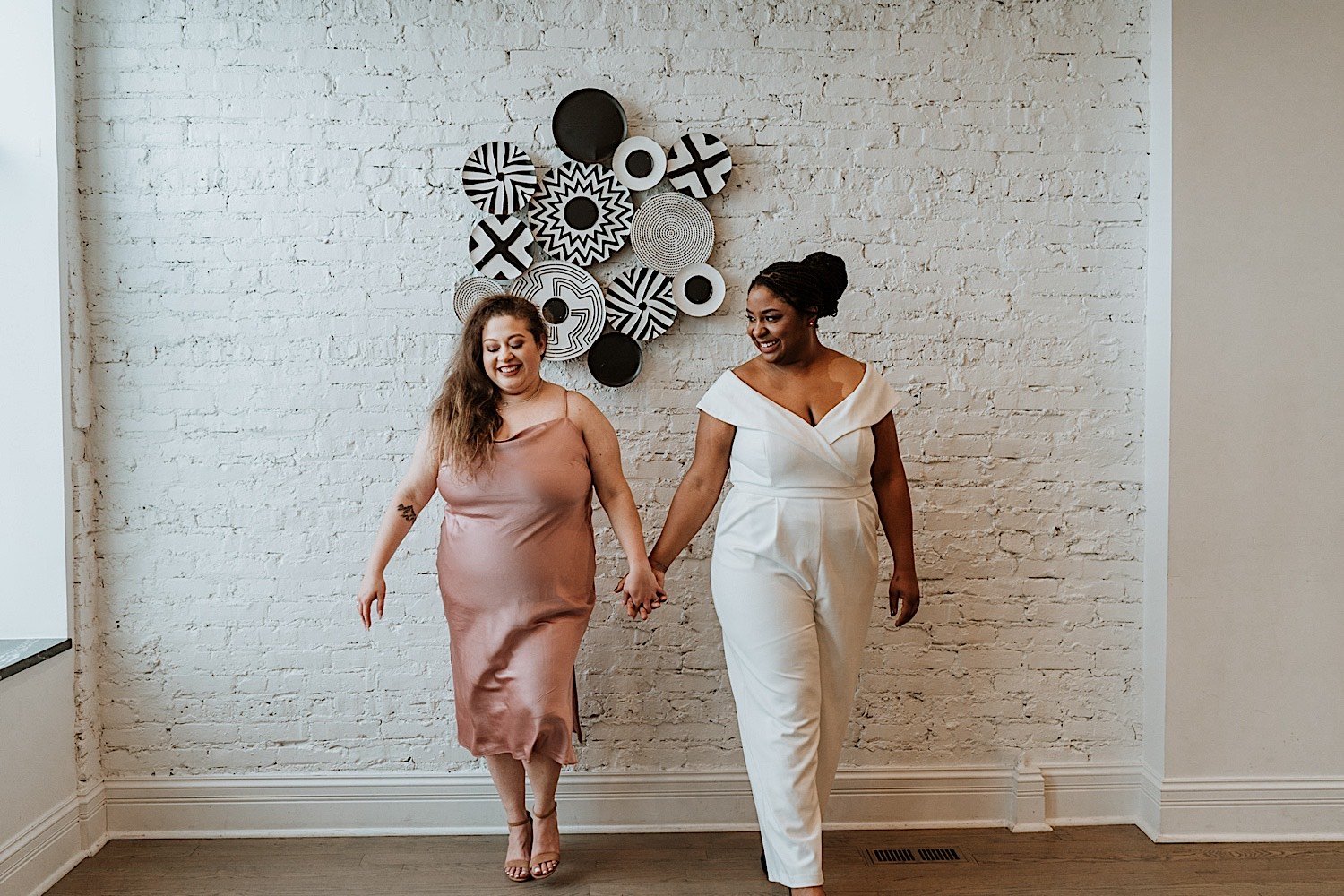 Brides hold hands in front of wall art during their Humboldt Park wedding