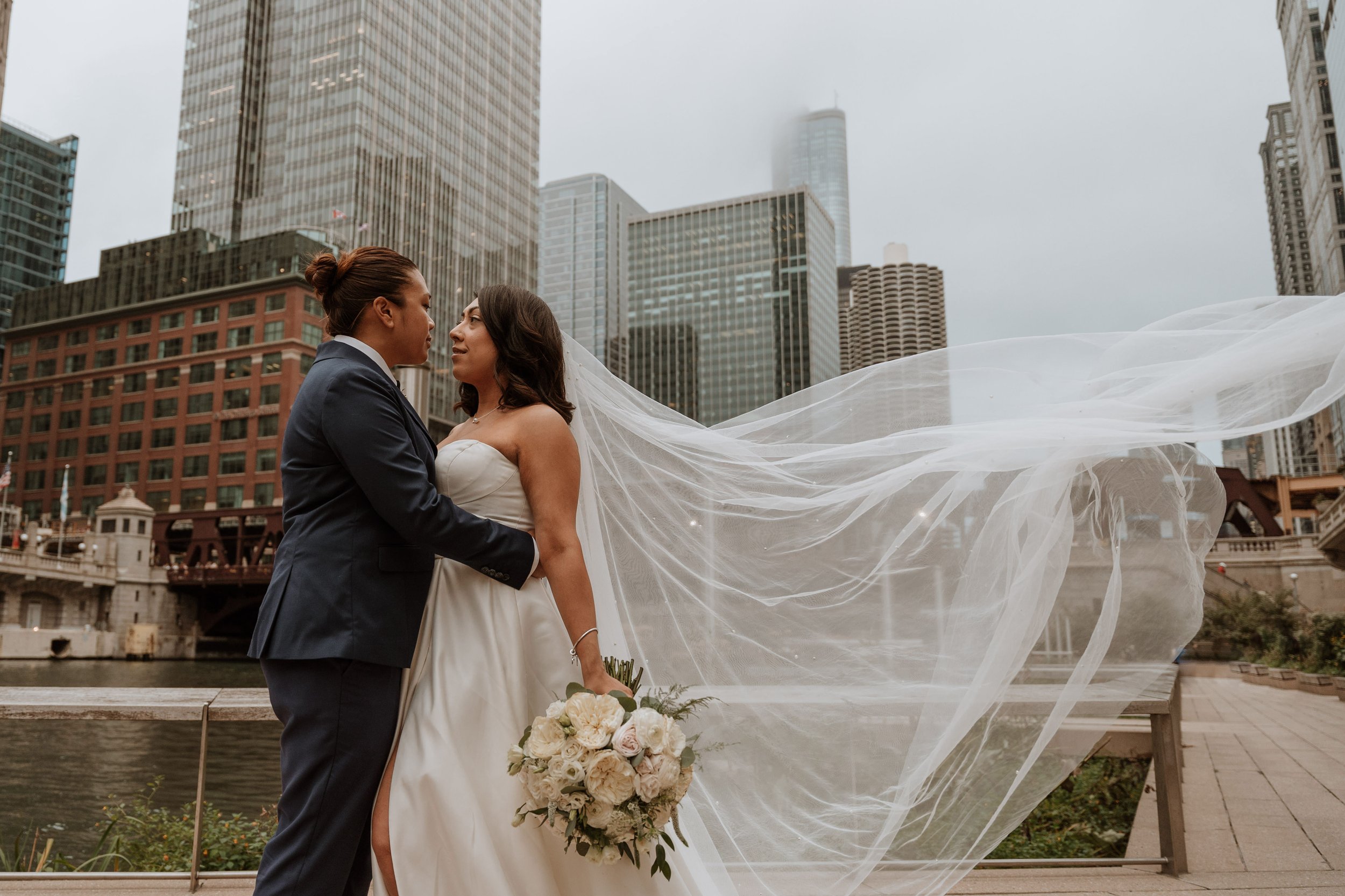 Newlywed couple stand in front of Chicago river and skyline with veil blowing in the wind