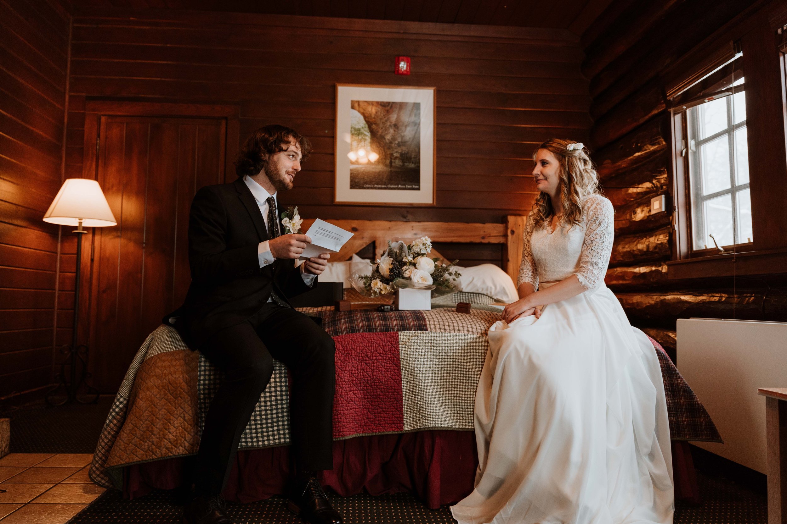 Couple sit on bed in log cabin and read vows privately to one another before their wedding