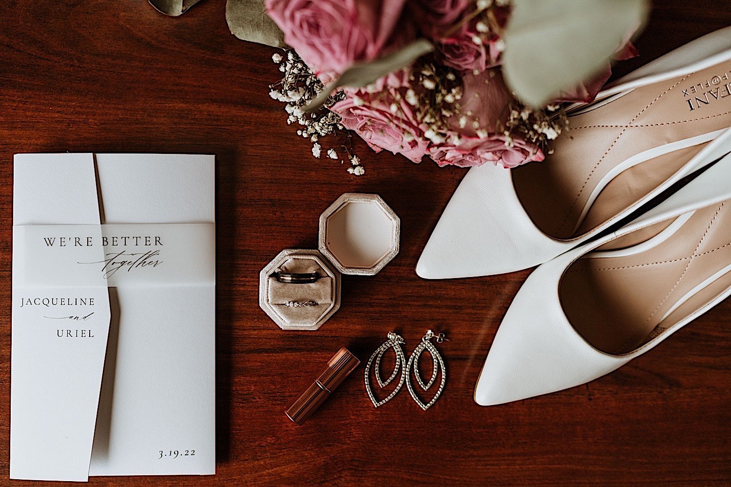 Photo of wedding rings, earrings, shoes, flowers and a wedding invite on a table