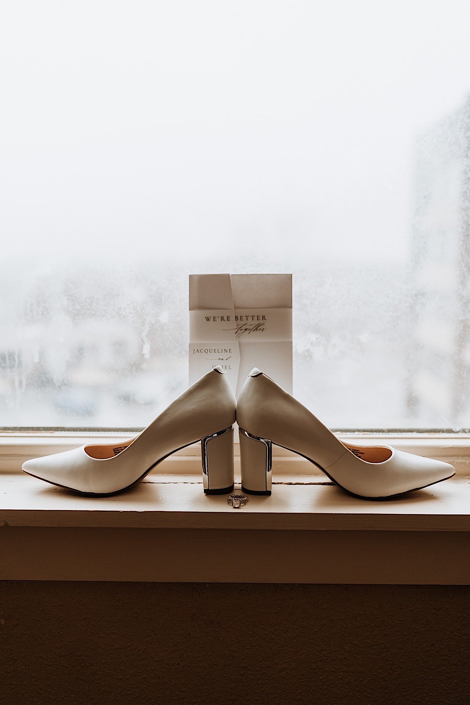 White shoes with a wedding invite behind them places in front of a window