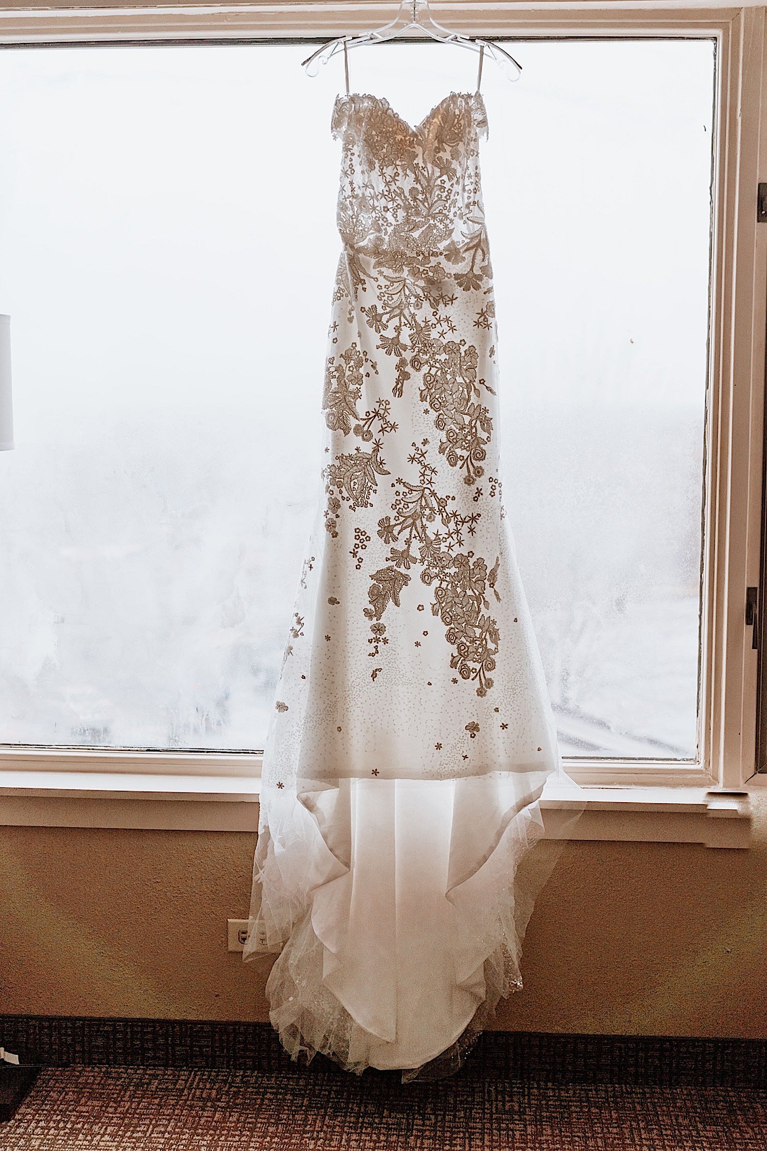 A wedding dress hanging in front of a window