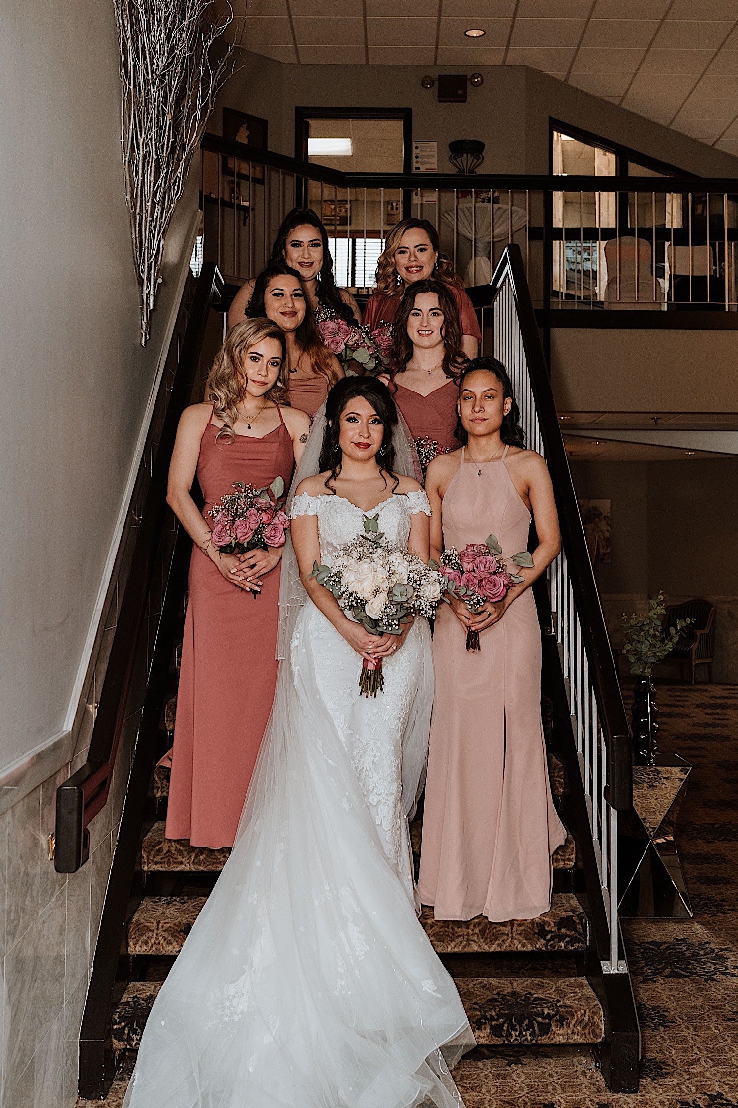 Bride poses with bridesmaids behind her on staircase prior to wedding