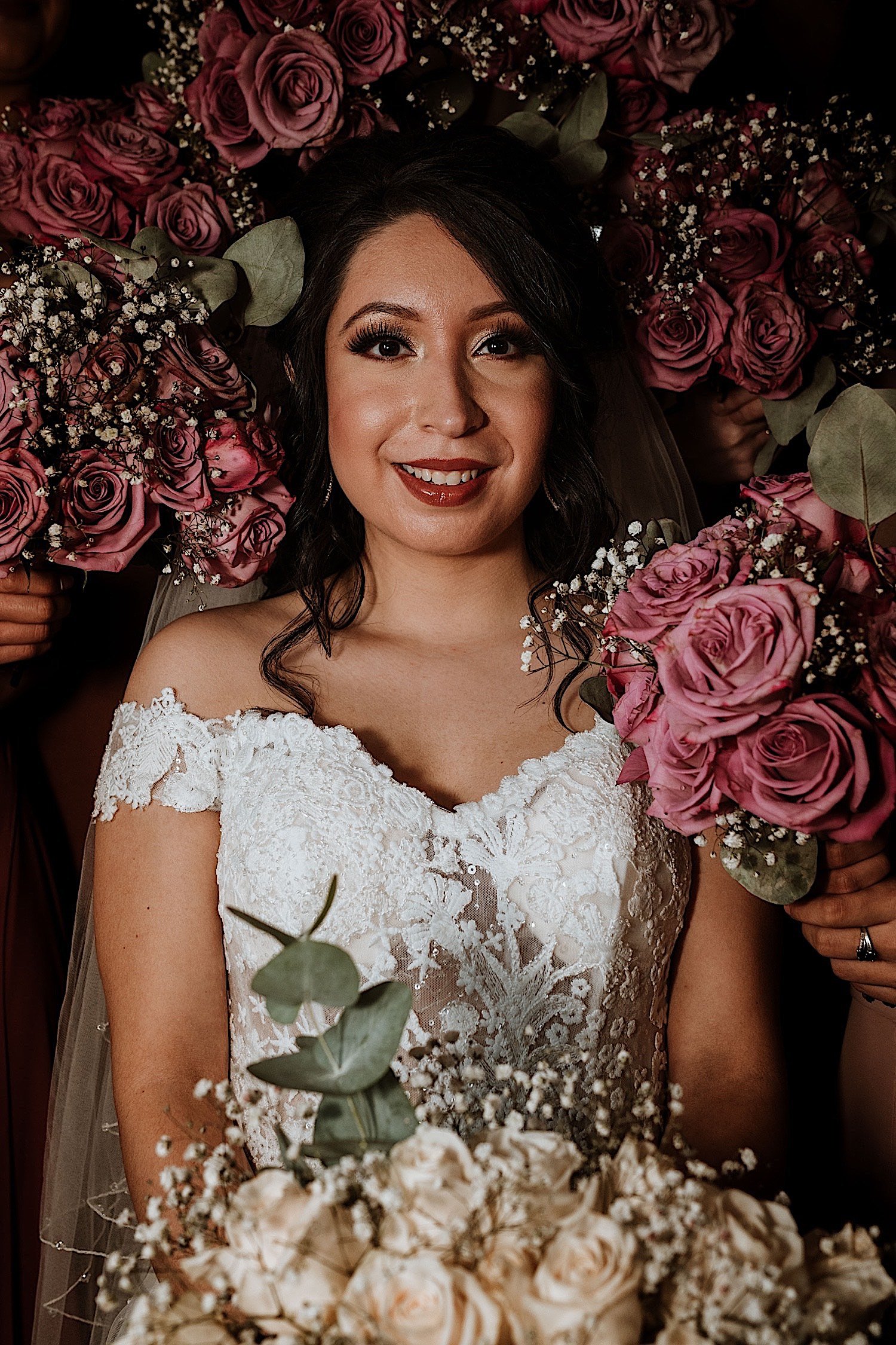 Bride smiles at the camera in her wedding dress surrounded by flowers
