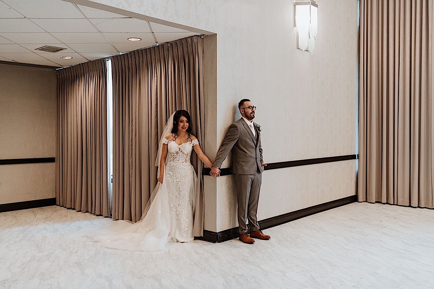 Bride and groom share first touch around a corner in their ballroom wedding venue