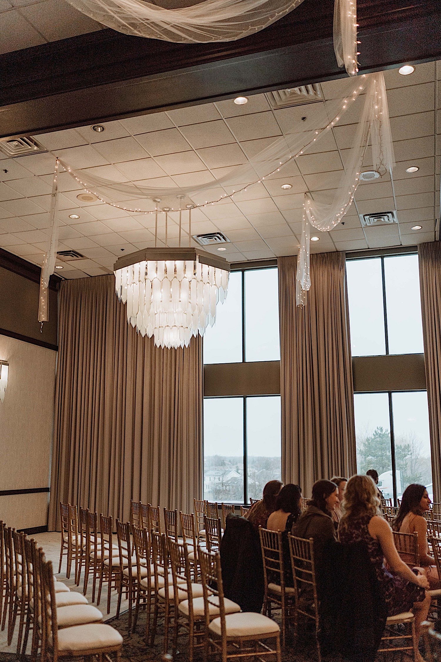 Guests seated in a ballroom for a wedding with a large glass chandelier overhead