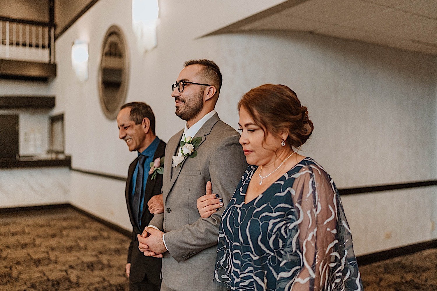 Groom enters Chicagoland ballroom wedding ceremony escorted by his mother and father