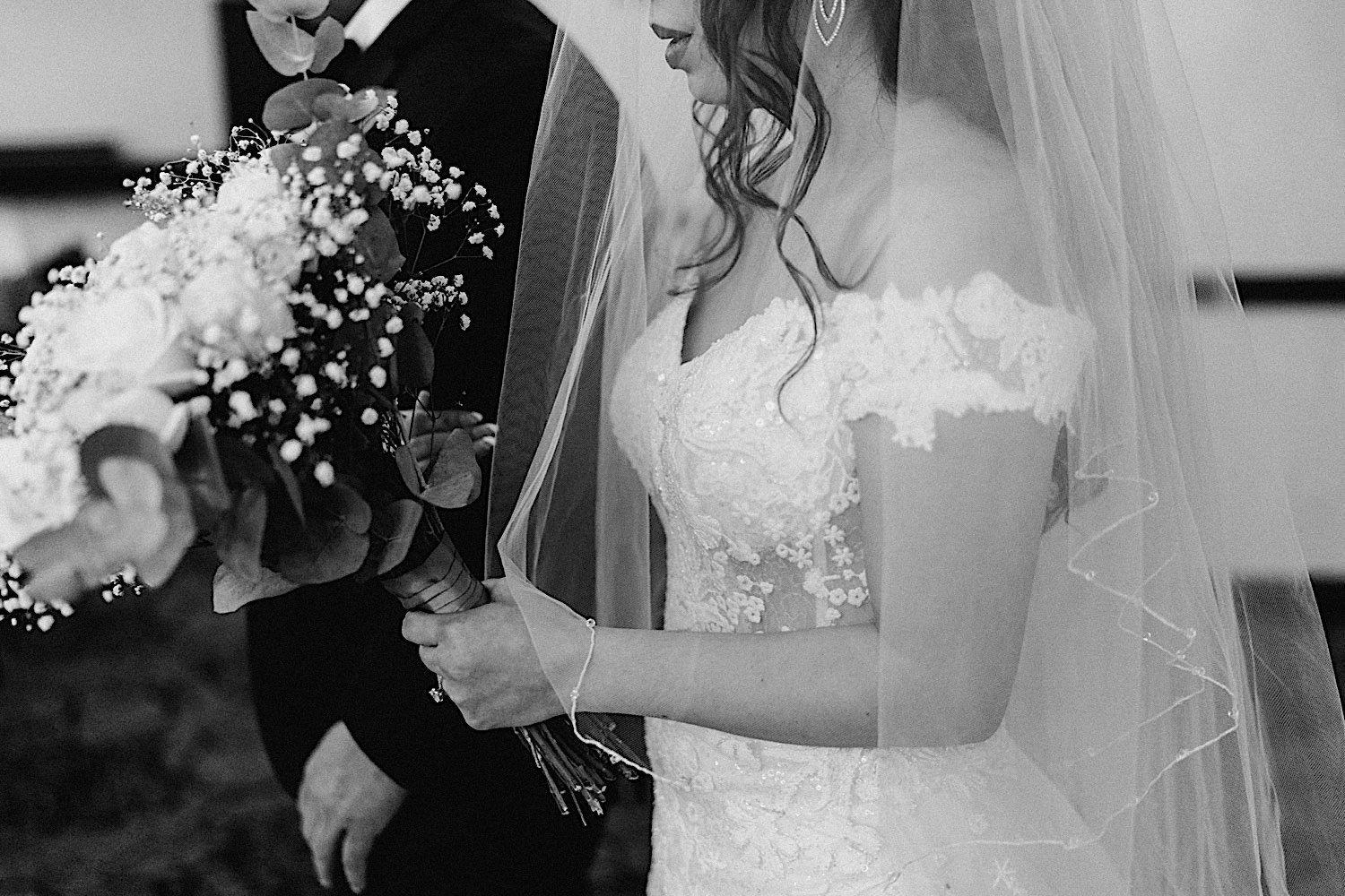 Black and white photo of a bride carrying a bouquet of flowers while being escorted down the aisle