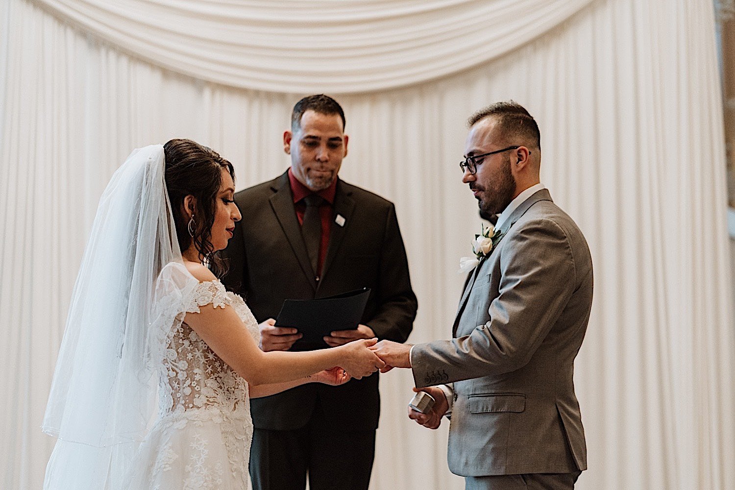 Bride and groom exchange rings during their wedding ceremony as the pastor watches