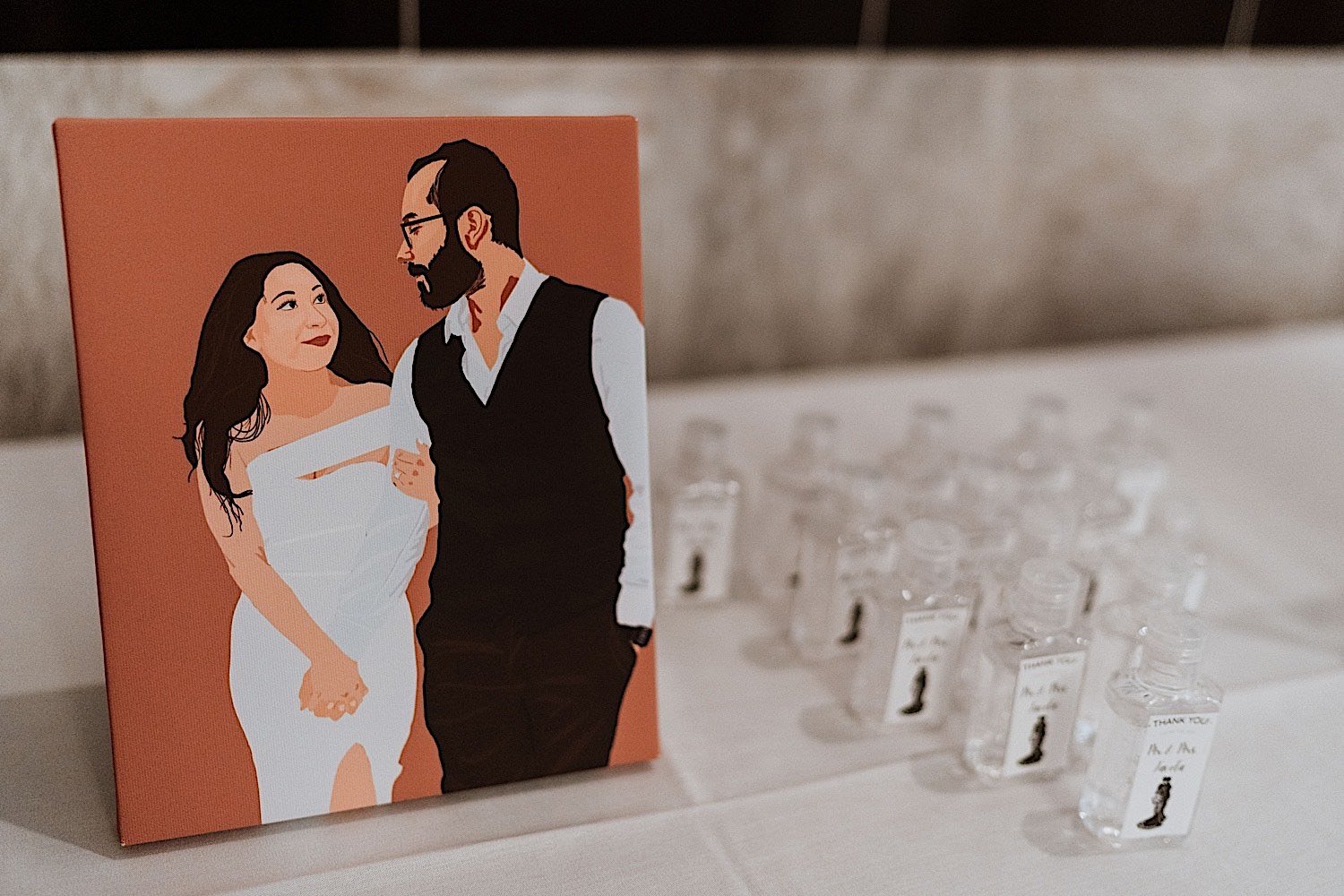 Painting of the bride and groom next to each other with hand sanitizer wedding favors next to the painting