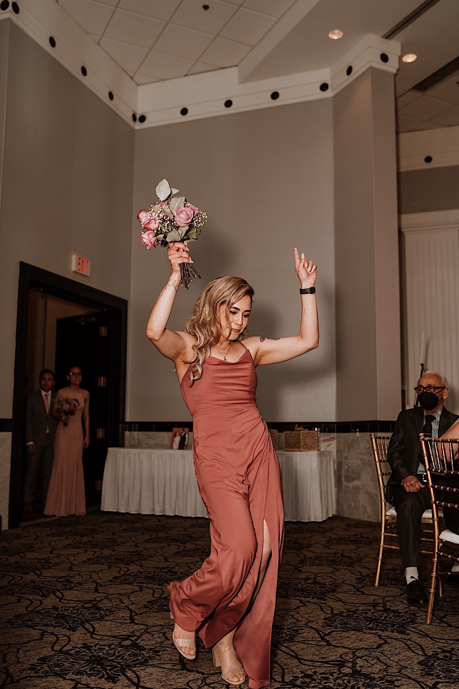 Bridesmaid enters ballroom wedding reception dancing while holding a bouquet