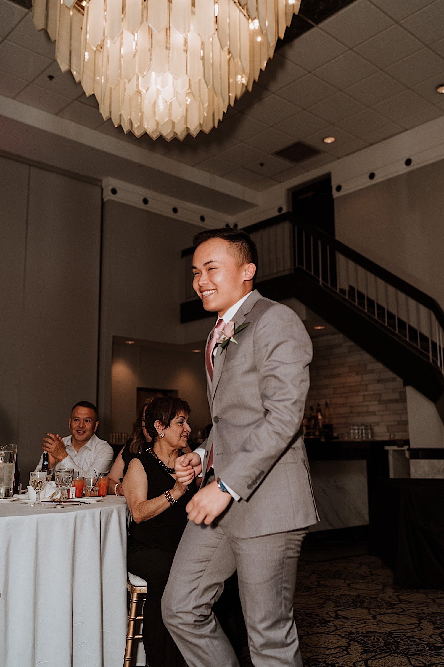 Groomsman smiles entering ballroom wedding reception with glass chandelier overhead