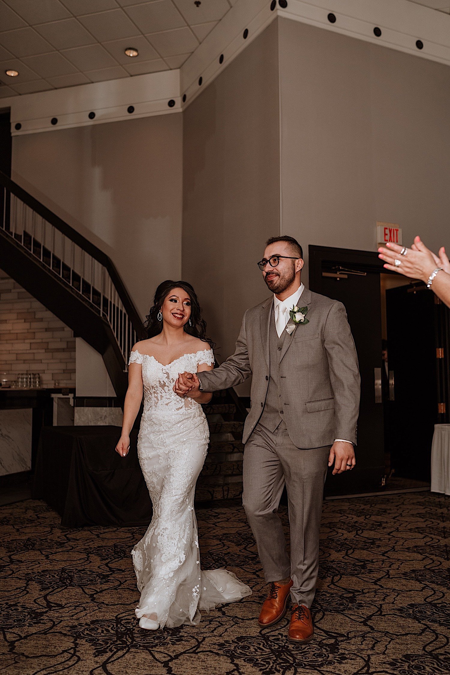 Bride and groom enter their Chicagoland ballroom wedding reception while holding hands and smiling at guests