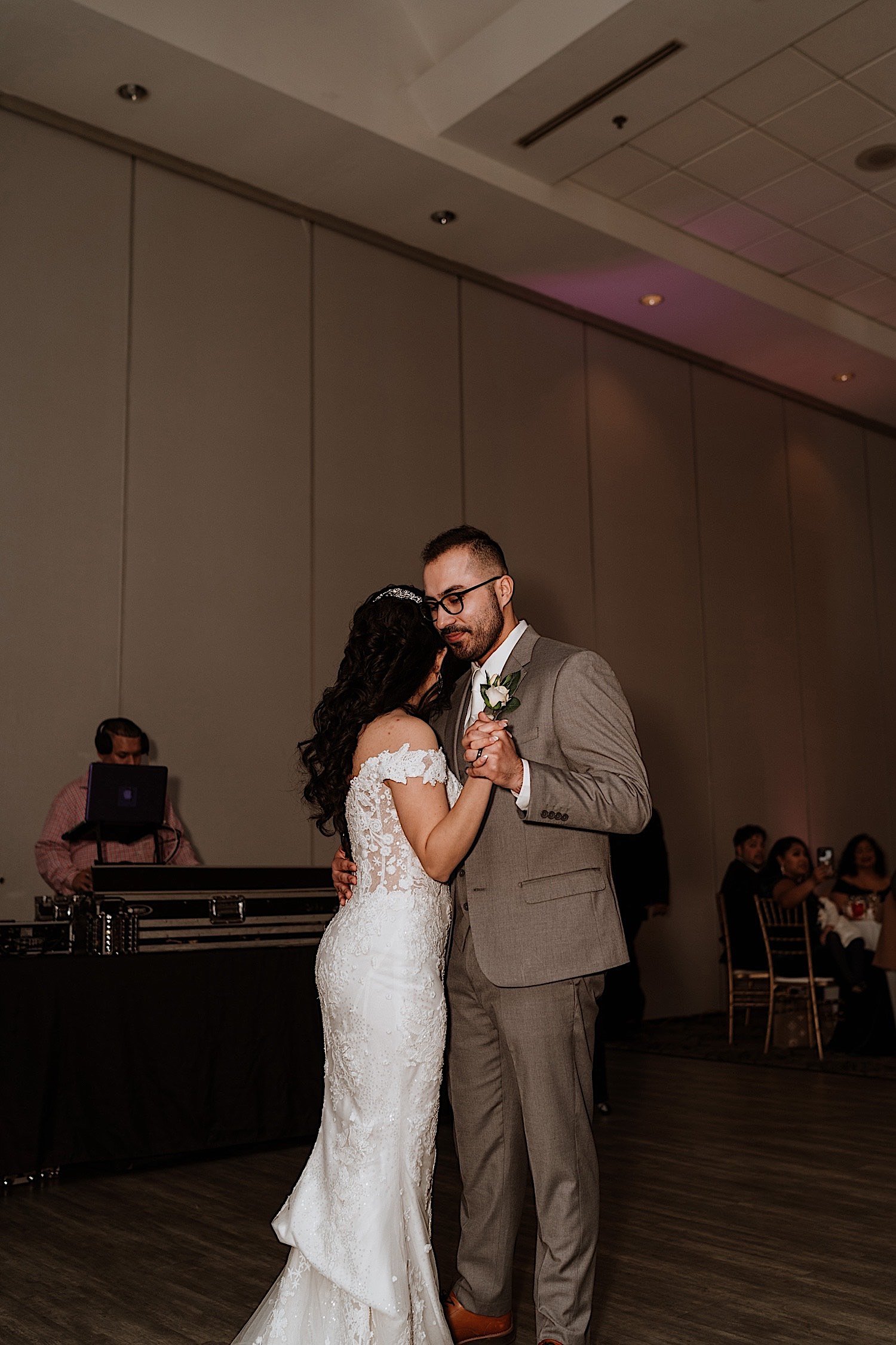 Bride and groom share first dance during wedding reception with guests and the DJ in the background