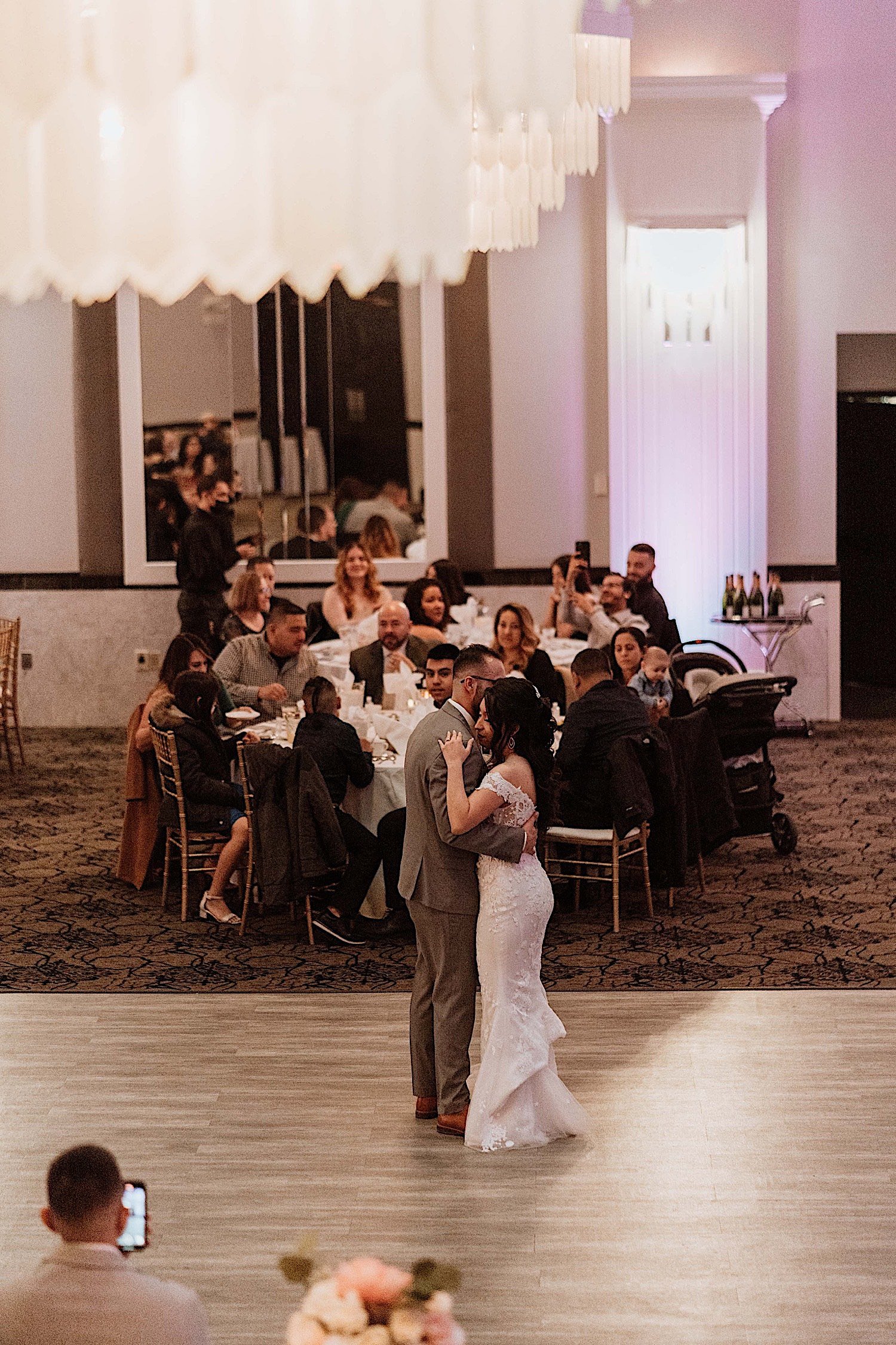 Bride and groom share first dance during wedding reception with guests watching in the background