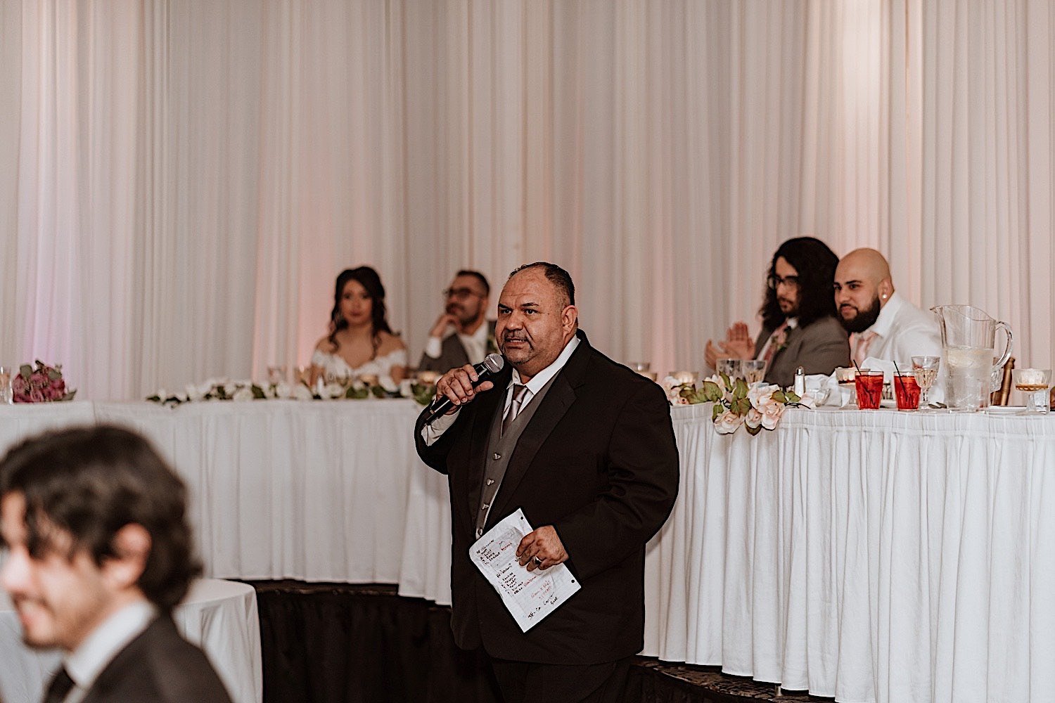 Man gives a toast during Chicagoland ballroom wedding reception with the bride and groom behind him