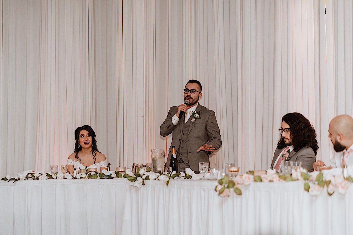 Groom gives a toast during Chicagoland ballroom wedding reception as bride and groomsmen are seated next to him