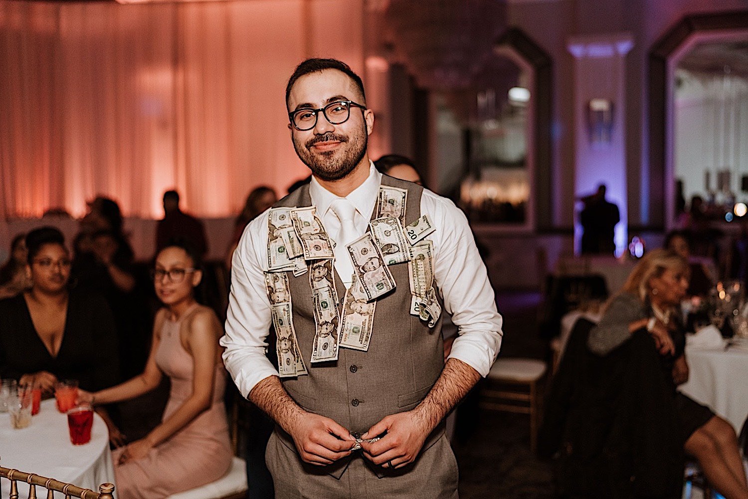 Groom smiles at camera during wedding reception with money pinned to his vest during Chicagoland ballroom wedding reception