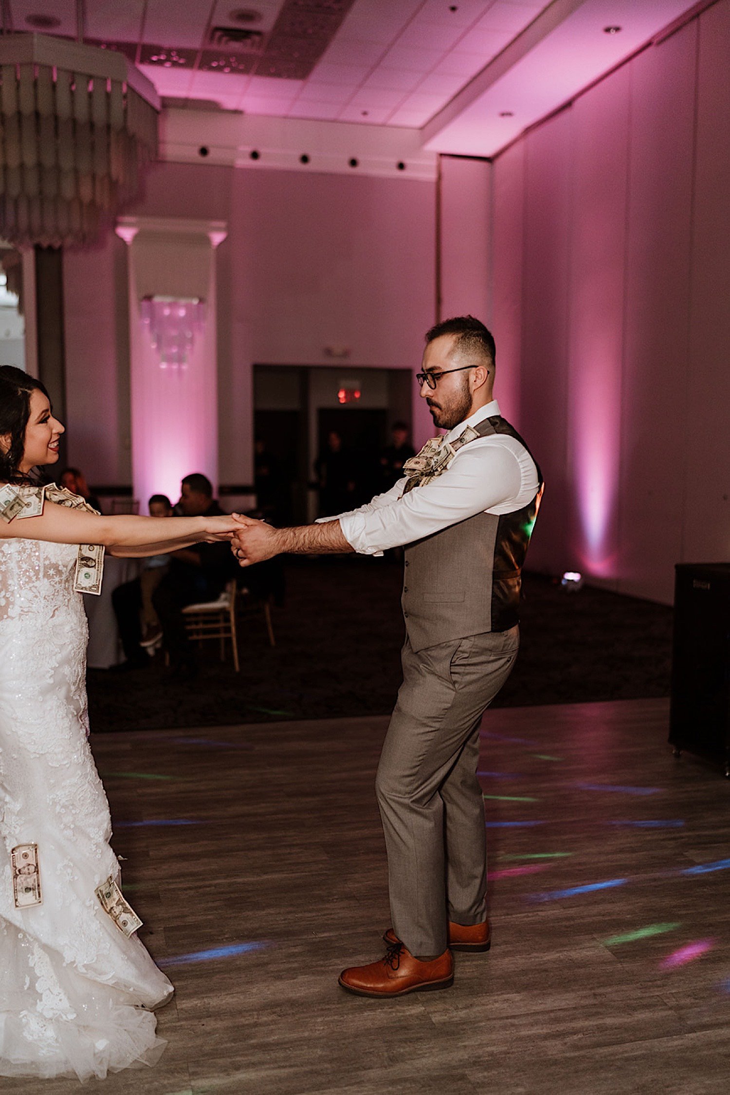 Bride and groom dance together during wedding reception with money pinned to them