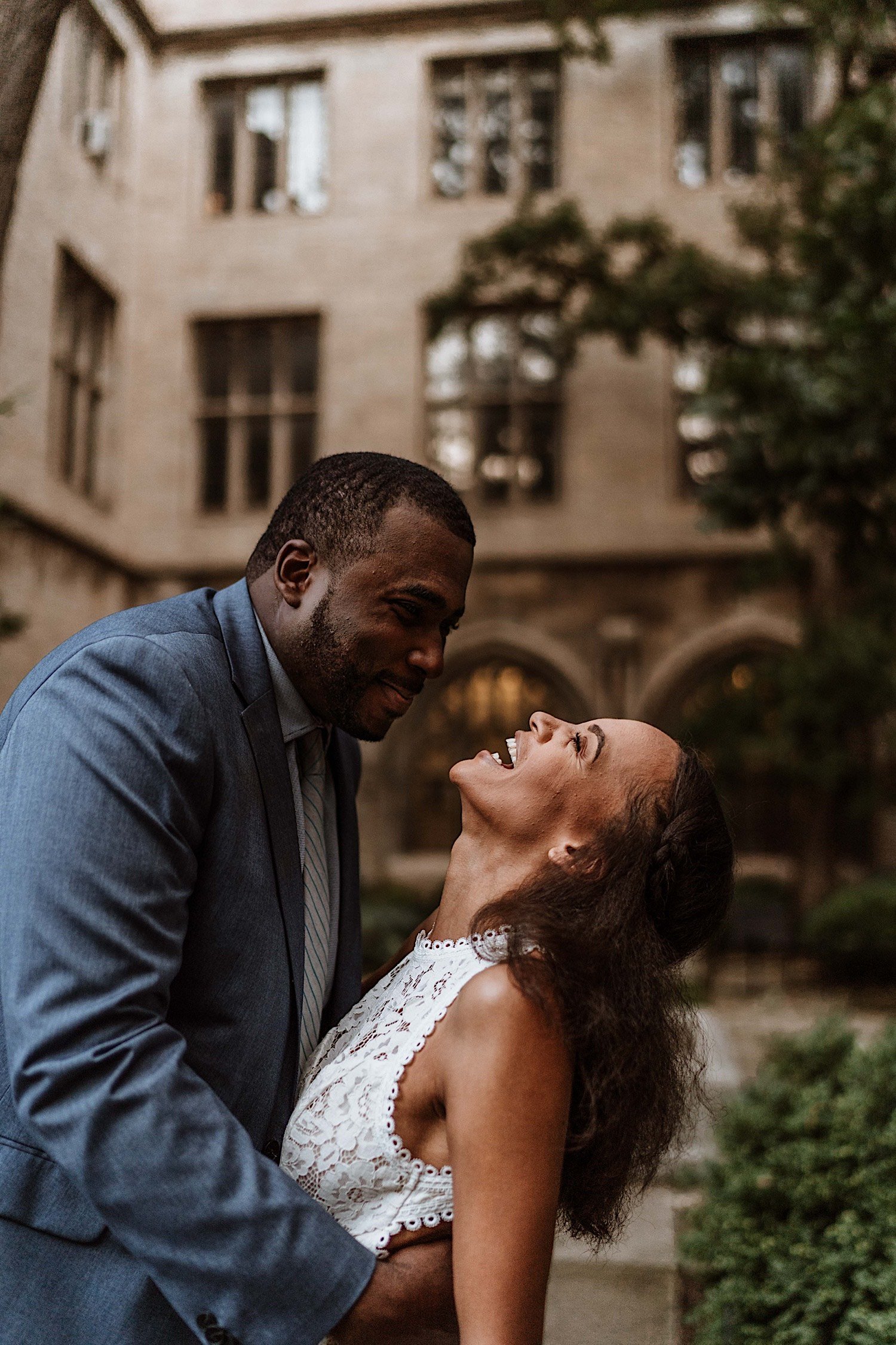 Groom holds bride as she laughs in University of Chicago campus