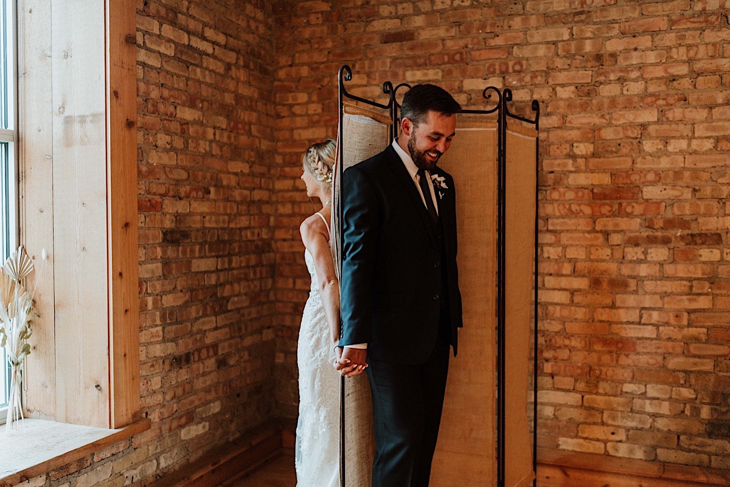 Bride and groom share first touch with a divider between them and a brick wall background