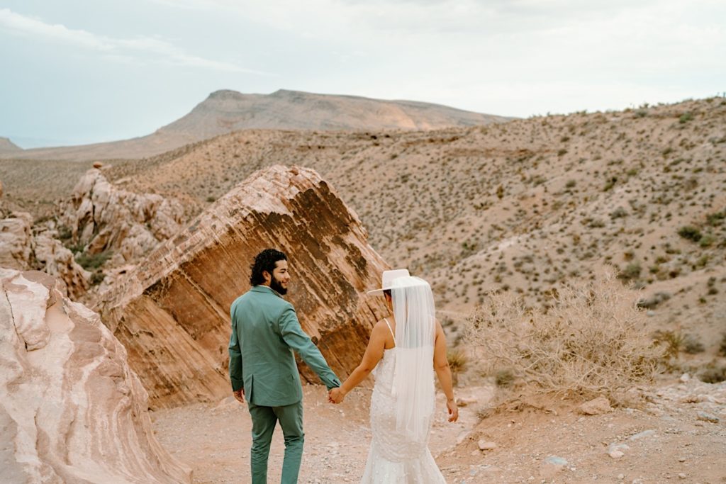 A bride and groom walk together through the red rocks the night before their elopement ceremony.