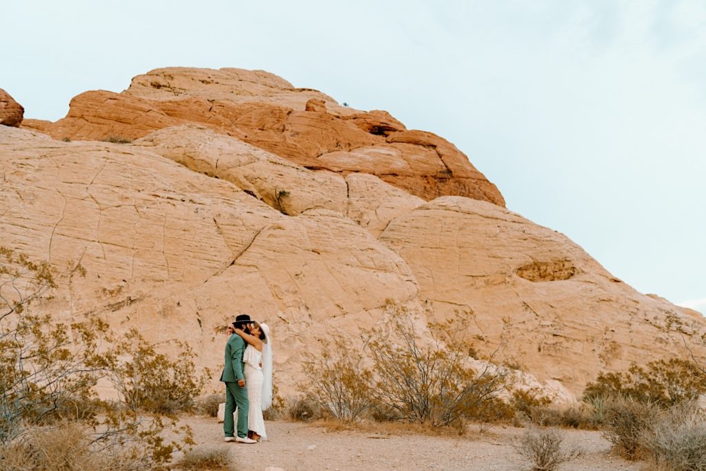 A wide photograph of a couple standing in front of a red rock mountain during their Las Vegas elopement