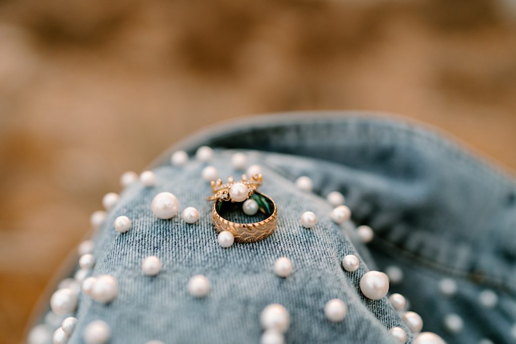 The brides wedding and engagement ring sitting on the brides denim jacket with pearls.