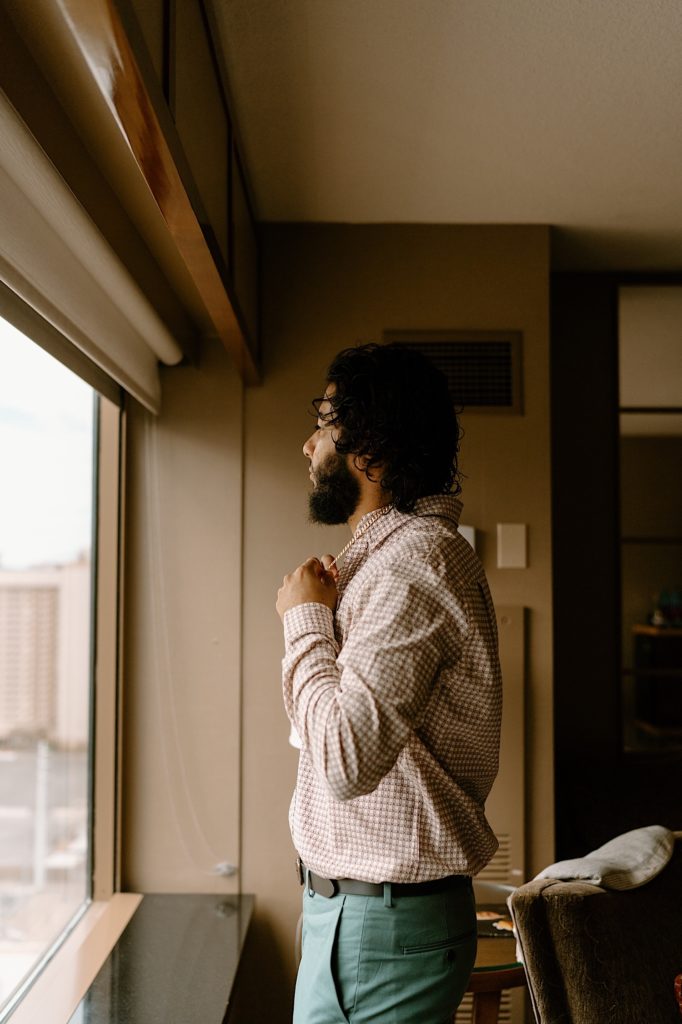 The groom gets ready for his Las Vegas elopement in his hotel room, looking out the window.