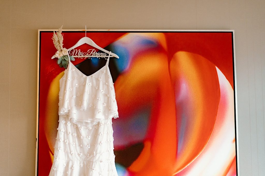 A white wedding dress hangs on a colorful painting in a Las Vegas hotel room