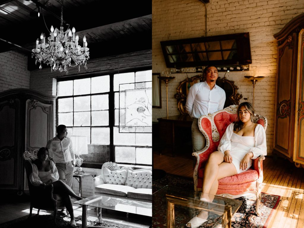 A fiancée sits in an ornate pink chair while her fiancé stands behind her.  They're next to a large window with stained glass during their engagement session at Salvage One.