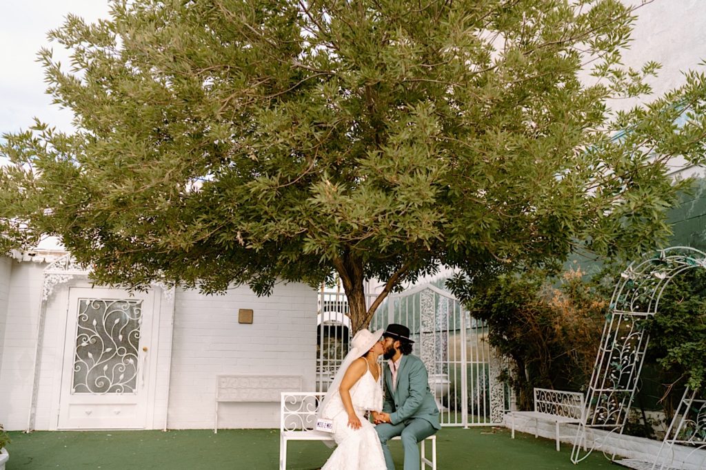 A bride and groom sit on a bench in the courtyard of the White Little Chapel in Las Vegas Nevada.