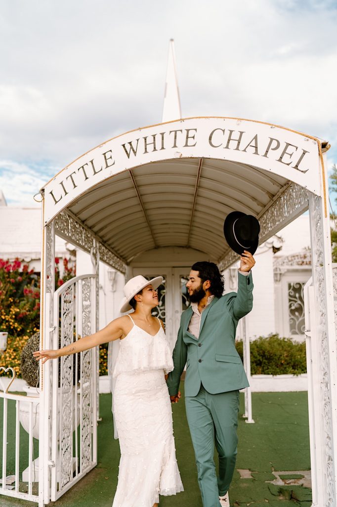 A bride and groom stand under the entrance of the Little White Chapel celebrating their elopement