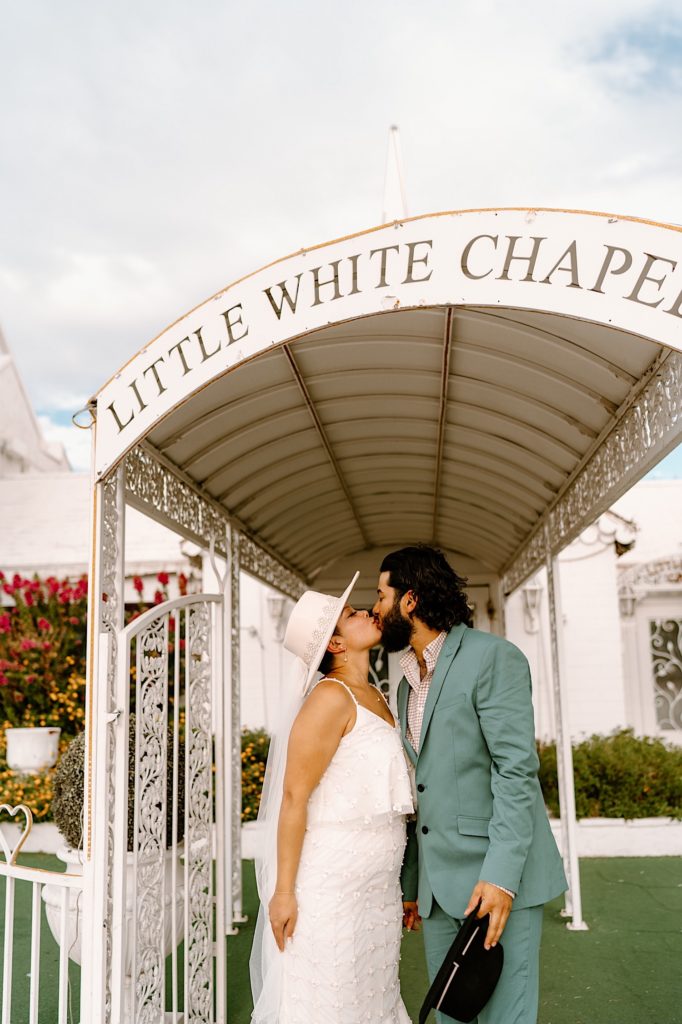 A bride and groom kiss under the entrance of the Little White Chapel celebrating their elopement