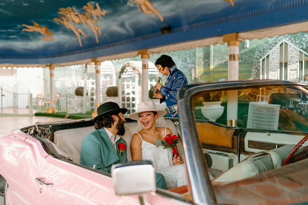 The bride and groom sit in the pink convertible laughing while Elvis begins their marriage ceremony.  