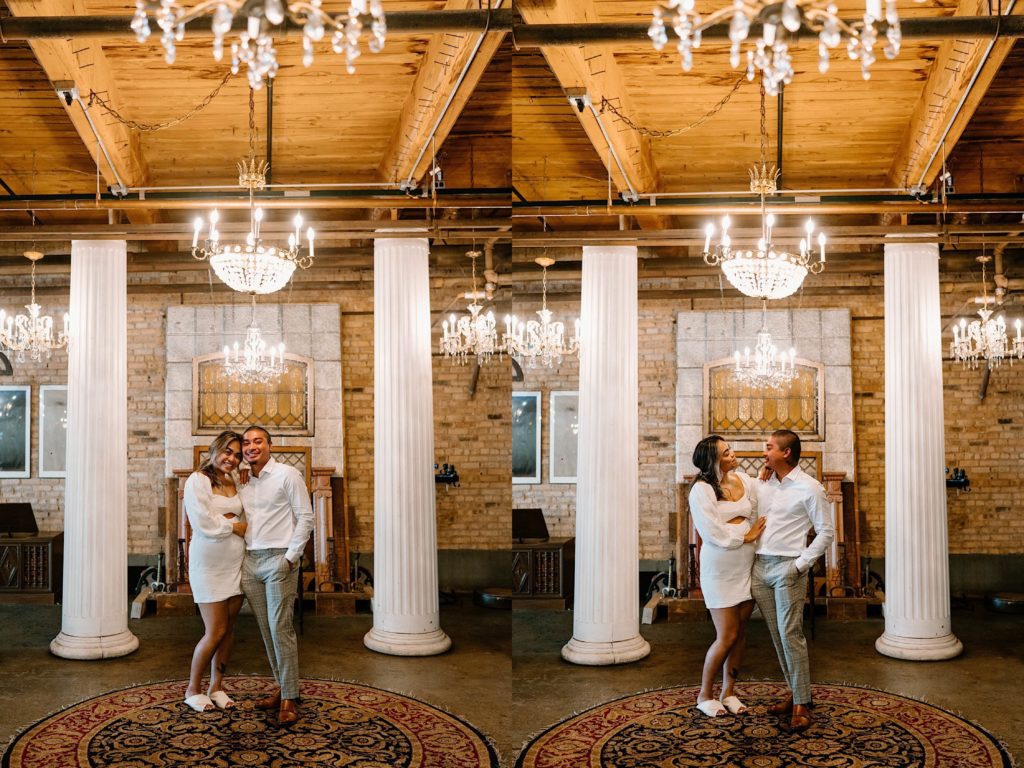 A couple stands under chandeliers and between two grecian pillars at Salvage One wedding venue in Chicago for their engagement session.