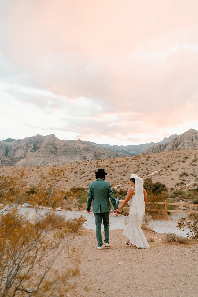 A bride and groom walk through the desert in Las Vegas Nevada while watching the sun set.