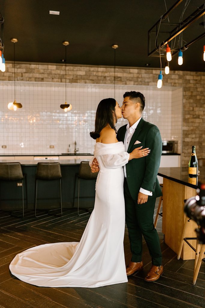 A bride and groom hold one another and kiss by the bar of their Airbnb.