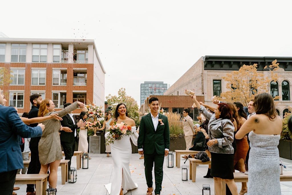 The bride and groom hold hands leaving their ceremony space on a rooftop at Loft Lucia in Chicago.