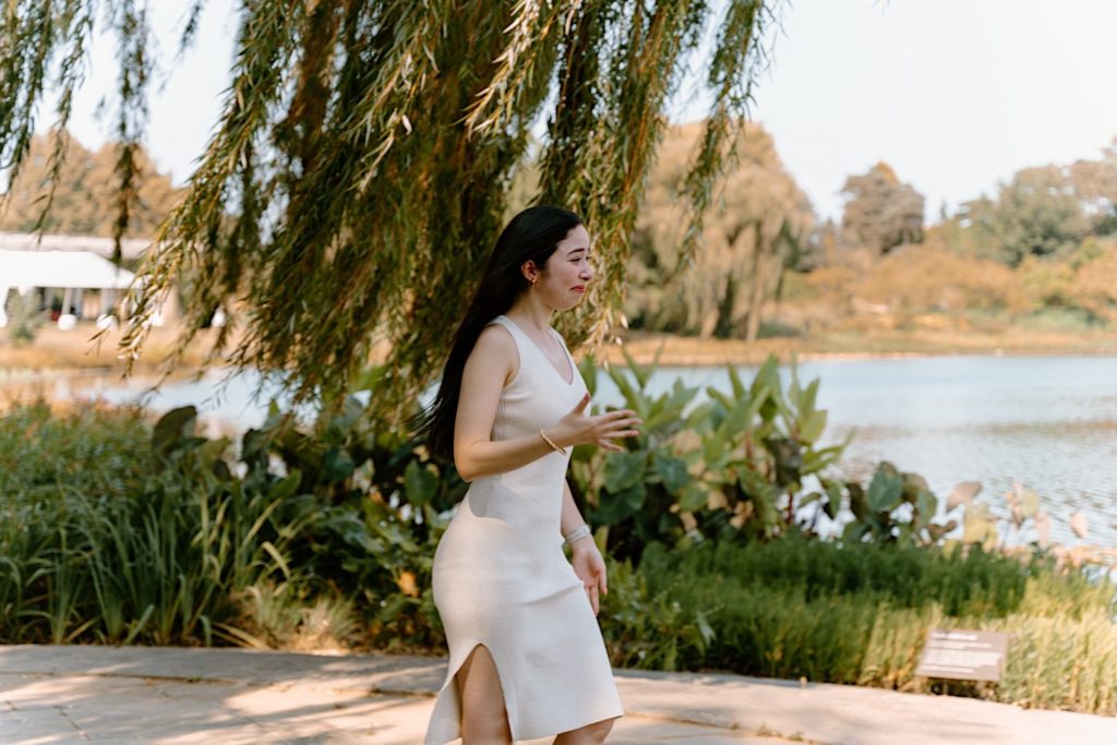 His bride Yesi walks towards him in the distance as he waits to propose to her on a stone path at the Chicago Botanic Garden.
