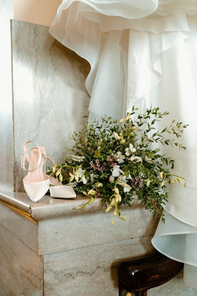 A bouquet and white flowers sitting on a marble staircase with the brides white shoes.  