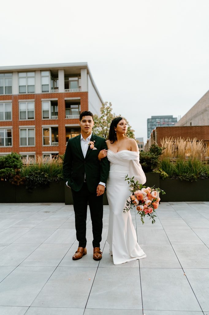 The bride and groom hold one another and stand looking away from one another at their rooftop wedding venue.