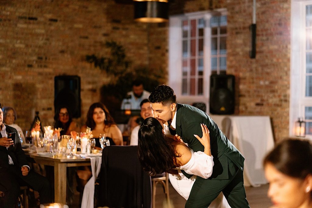 The bride and groom share their first dance on their wedding day at Loft Lucia.  The groom dips his bride and kisses her in front of their guests.