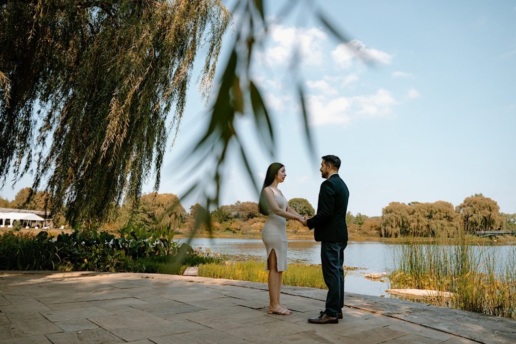 A couple holds hands facing one another overlooking a pond on a beautiful clear sky day in the Chicago Botanic Gardens