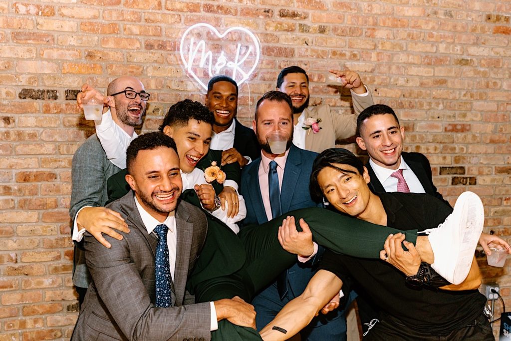 The groom is held by his friends while taking a fun photo at his wedding reception.