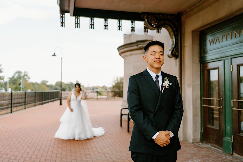 A bride standing behind the groom before their first look standing underneath the overhand at Joliet's Union Station.