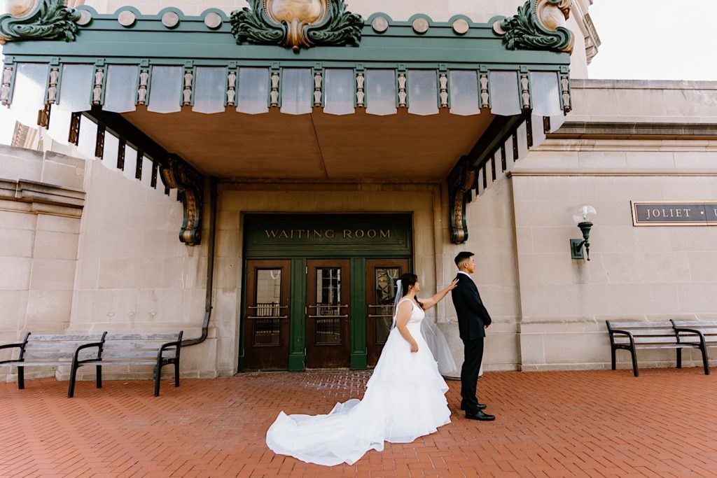 A bride standing behind the groom before their first look standing underneath the overhand at Joliet's Union Station.