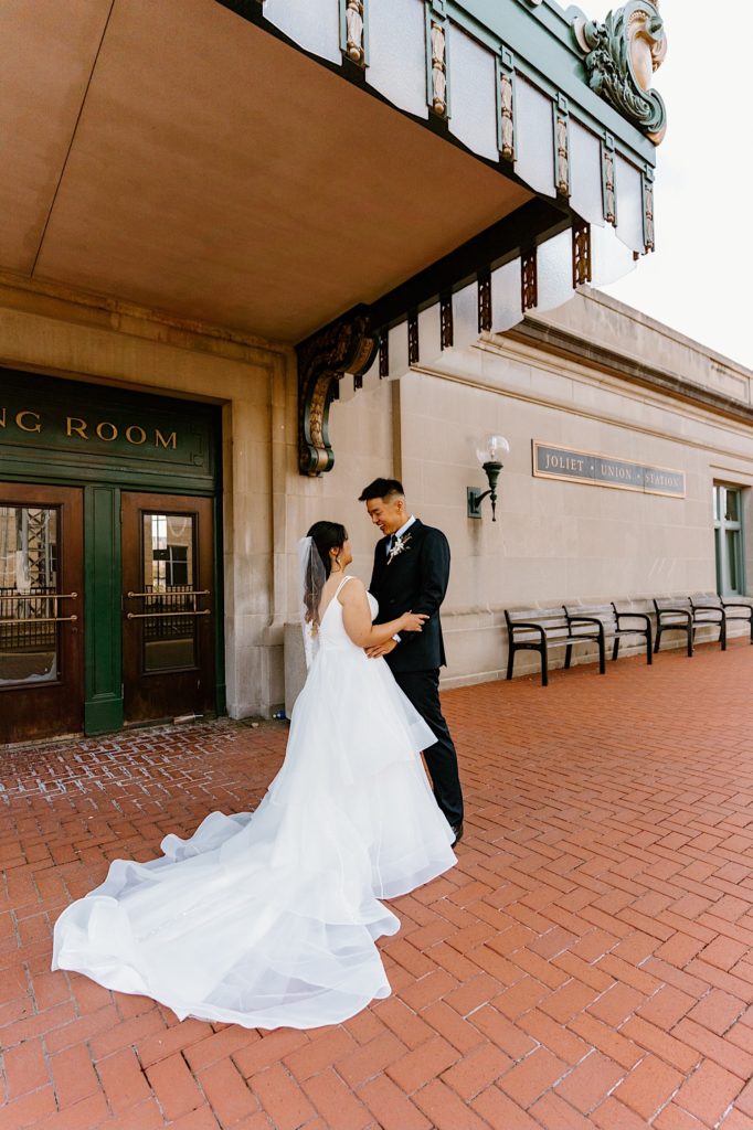 A bride and groom stand holding one another during their first look standing underneath the overhand at Joliet's Union Station.
