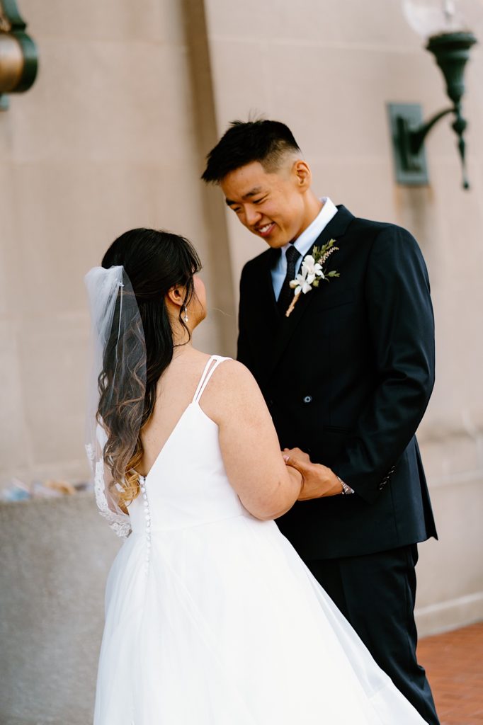 A bride and groom stand holding one another during their first look standing underneath the overhand at Joliet's Union Station.