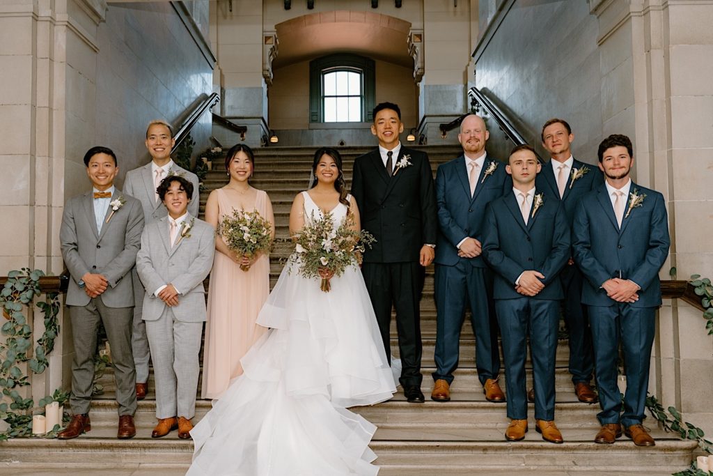 A bride and groom and their wedding party posing for portraits on the staircase at Joliet's Union Station.